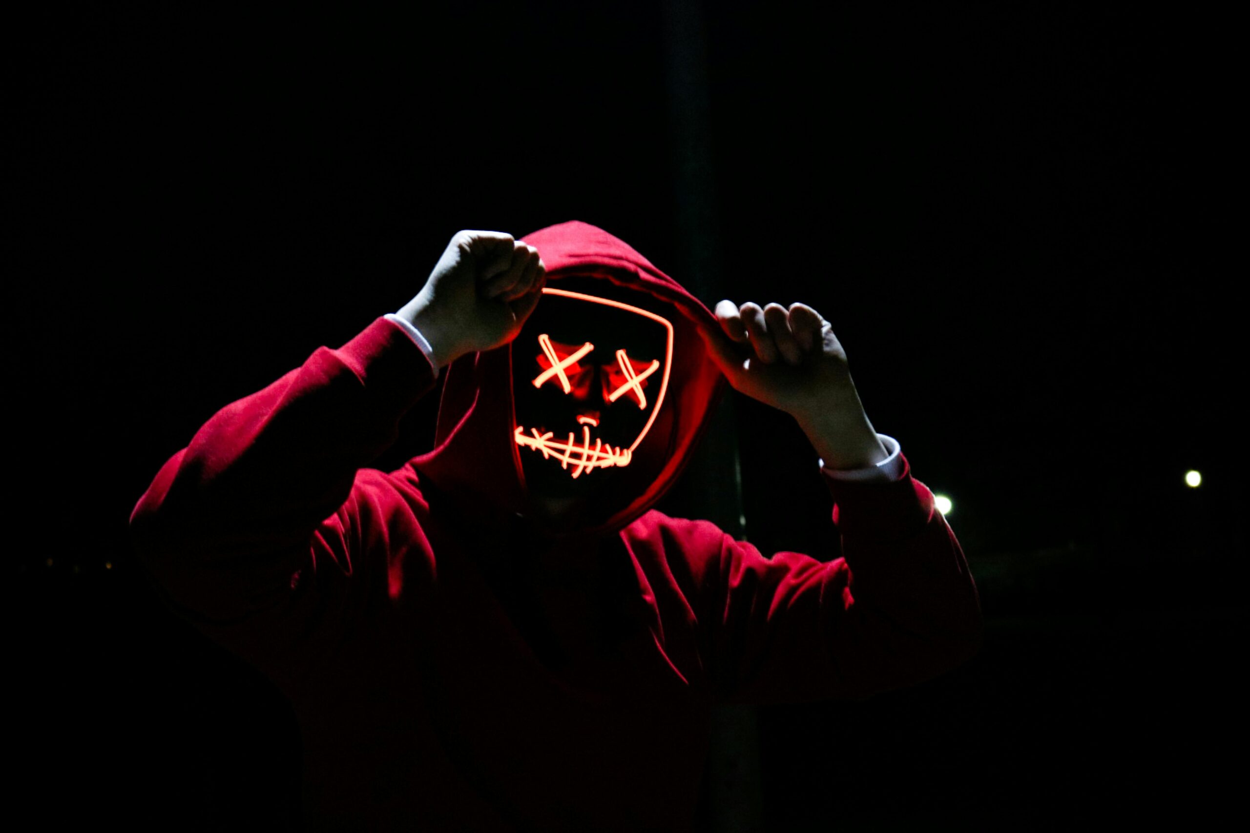 Main-home A spooky illuminated mask figure with a red hoodie in a dark setting, perfect for Halloween themes.